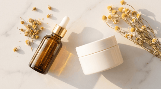 Amber glass dropper bottle and cream jar on marble surface with chamomile flowers — K-beauty retinal skincare editorial